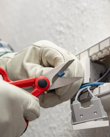 Electrician worker at work with scissors prepares the electrical cables of an electrical system. Working safely with protective gloves. Construction industry.の写真素材
