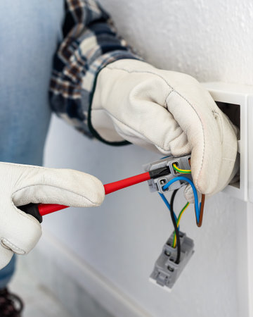 Electrician worker with screwdriver fixes electrical wires in the terminals of the socket of an electrical system. Working safely with protective gloves. Construction industry.の写真素材
