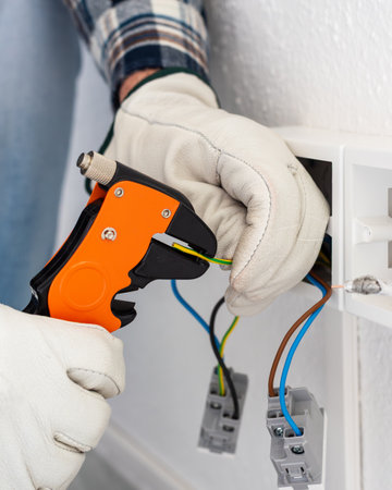 Electrician worker at work with wire stripper pliers prepares the electrical cables of an electrical system. Working safely with protective gloves. Construction industry.の写真素材