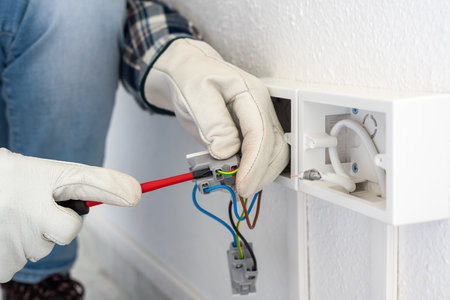 Electrician worker with screwdriver fixes electrical wires in the terminals of the socket of an electrical system. Working safely with protective gloves. Construction industry.の写真素材