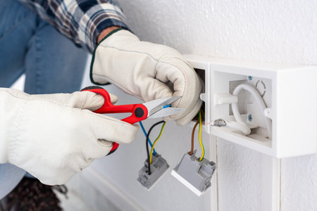 Electrician worker at work with scissors prepares the electrical cables of an electrical system. Working safely with protective gloves. Construction industry.の写真素材