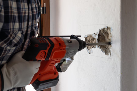 Carpenter electrician with demolition hammer prepares the cavity in the wall where to insert the built-in electrical panel. Work safely with protective gloves. Construction industry.の写真素材