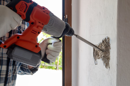 Carpenter electrician with demolition hammer prepares the cavity in the wall where to insert the built-in electrical panel. Work safely with protective gloves. Construction industry.の写真素材