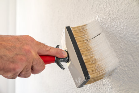 Close-up of a hand. A painter paints a masonry wall with white paint using using the paintbrush....