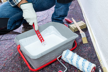 Close-up of hand wearing protective gloves. A painter prepares the white paint to whitewash the...