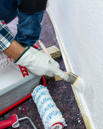 Close-up of hand wearing protective gloves. House painter worker paints a masonry wall with white paint using the paintbrush. Construction industry. Safety at Work.の写真素材