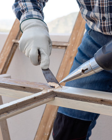 Carpenter using heat gun and wood scraper removes paint from old wooden window. Construction industry, carpentry. Restoration.の写真素材