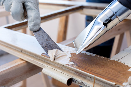 Carpenter using heat gun and wood scraper removes paint from old wooden window. Construction industry, carpentry. Restoration.の写真素材