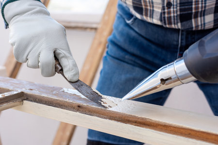 Carpenter using heat gun and wood scraper removes paint from old wooden window. Construction industry, carpentry. Restoration.の写真素材