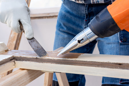 Carpenter using heat gun and wood scraper removes paint from old wooden window. Construction industry, carpentry. Restoration.の写真素材