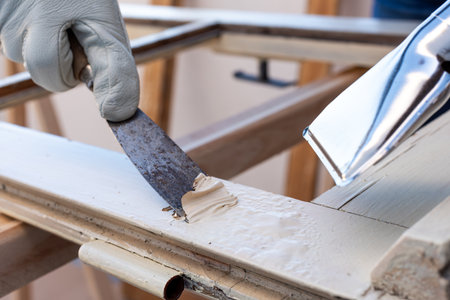Carpenter using heat gun and wood scraper removes paint from old wooden window. Construction industry, carpentry. Restoration.の写真素材