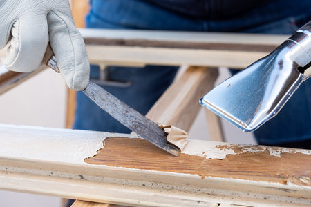 Carpenter using heat gun and wood scraper removes paint from old wooden window. Construction industry, carpentry. Restoration.の写真素材