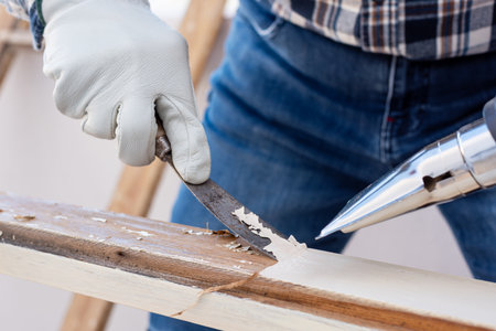 Carpenter using heat gun and wood scraper removes paint from old wooden window. Construction industry, carpentry. Restoration.の写真素材