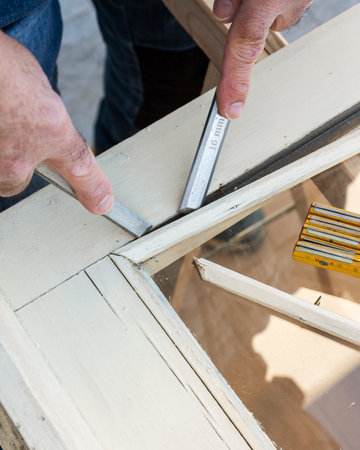 Carpenter using chisels removes the wooden frame blocking the glass from an old wooden window. Construction industry, carpentry. Restoration.の写真素材