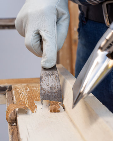 Carpenter using heat gun and wood scraper removes paint from old wooden window. Construction industry, carpentry. Restoration.の写真素材