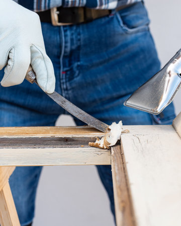 Carpenter using heat gun and wood scraper removes paint from old wooden window. Construction industry, carpentry. Restoration.の写真素材