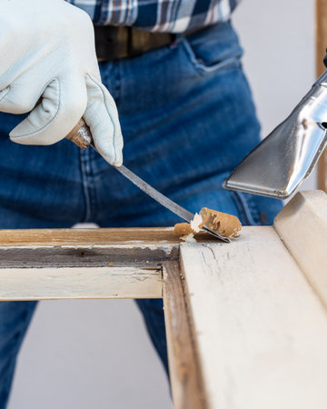 Carpenter using heat gun and wood scraper removes paint from old wooden window. Construction industry, carpentry. Restoration.の写真素材