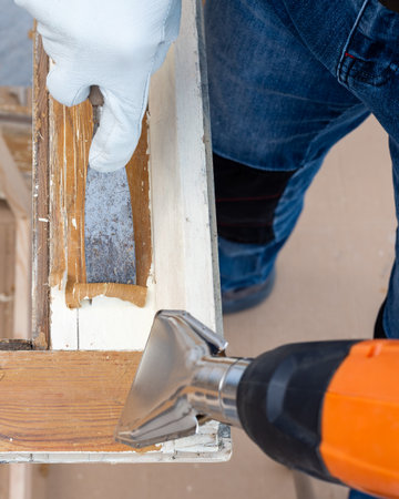 Carpenter using heat gun and wood scraper removes paint from old wooden window. Construction industry, carpentry. Restoration.の写真素材