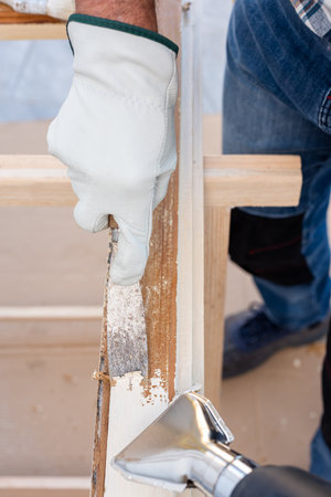 Carpenter using heat gun and wood scraper removes paint from old wooden window. Construction industry, carpentry. Restoration.の写真素材