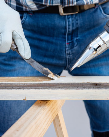 Carpenter using heat gun and wood scraper removes paint from old wooden window. Construction industry, carpentry. Restoration.の写真素材