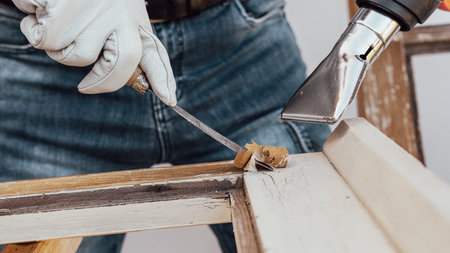 Carpenter using heat gun and wood scraper removes paint from old wooden window. Construction industry, carpentry. Restoration.の写真素材