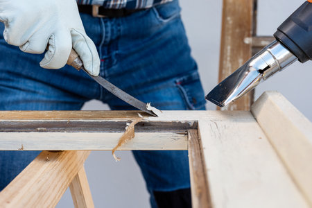 Carpenter using heat gun and wood scraper removes paint from old wooden window. Construction industry, carpentry. Restoration.の写真素材