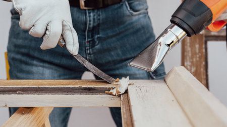 Carpenter using heat gun and wood scraper removes paint from old wooden window. Construction industry, carpentry. Restoration.の写真素材
