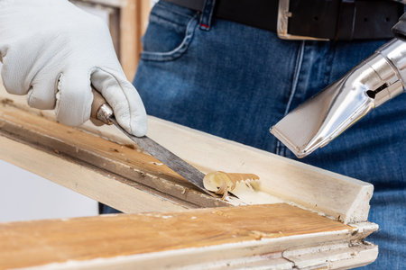 Carpenter using heat gun and wood scraper removes paint from old wooden window. Construction industry, carpentry. Restoration.の写真素材