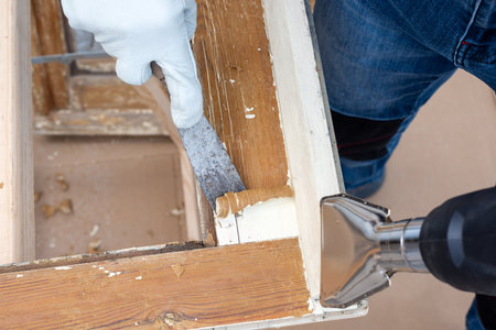 Carpenter using heat gun and wood scraper removes paint from old wooden window. Construction industry, carpentry. Restoration.の写真素材