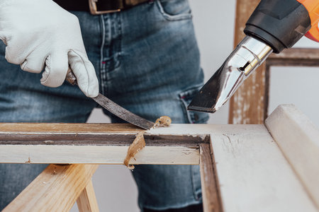 Carpenter using heat gun and wood scraper removes paint from old wooden window. Construction industry, carpentry. Restoration.の写真素材