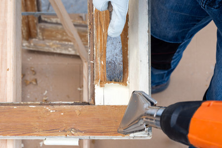 Carpenter using heat gun and wood scraper removes paint from old wooden window. Construction industry, carpentry. Restoration.の写真素材