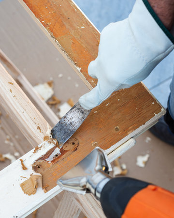 Carpenter using heat gun and wood scraper removes paint from old wooden window. Construction industry, carpentry. Restoration.の写真素材