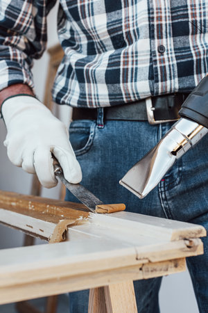 Carpenter using heat gun and wood scraper removes paint from old wooden window. Construction industry, carpentry. Restoration.の写真素材