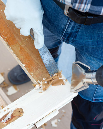 Carpenter using heat gun and wood scraper removes paint from old wooden window. Construction industry, carpentry. Restoration.の写真素材