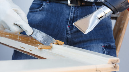 Carpenter using heat gun and wood scraper removes paint from old wooden window. Construction industry, carpentry. Restoration.の写真素材