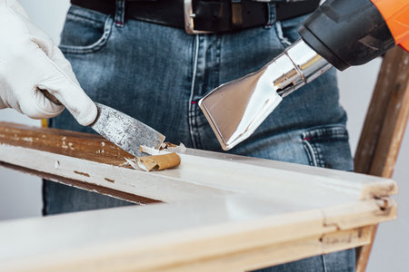 Carpenter using heat gun and wood scraper removes paint from old wooden window. Construction industry, carpentry. Restoration.の写真素材