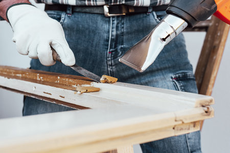 Carpenter using heat gun and wood scraper removes paint from old wooden window. Construction industry, carpentry. Restoration.の写真素材