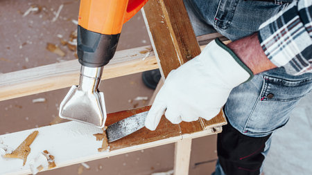 Carpenter using heat gun and wood scraper removes paint from old wooden window. Construction industry, carpentry. Restoration.の写真素材