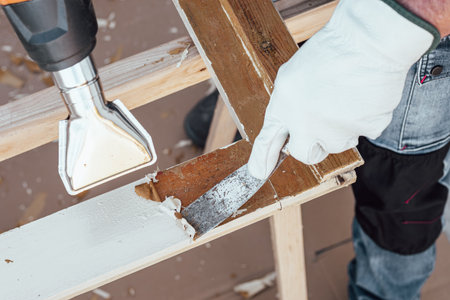 Carpenter using heat gun and wood scraper removes paint from old wooden window. Construction industry, carpentry. Restoration.の写真素材
