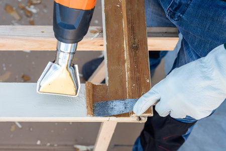 Carpenter using heat gun and wood scraper removes paint from old wooden window. Construction industry, carpentry. Restoration.の写真素材