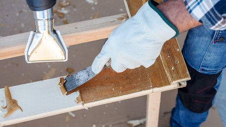 Carpenter using heat gun and wood scraper removes paint from old wooden window. Construction industry, carpentry. Restoration.の写真素材
