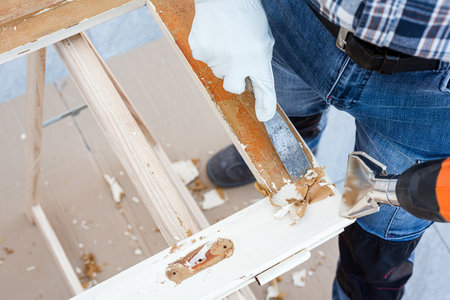 Carpenter using heat gun and wood scraper removes paint from old wooden window. Construction industry, carpentry. Restoration.の写真素材