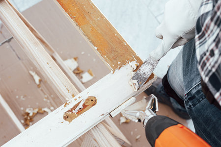 Carpenter using heat gun and wood scraper removes paint from old wooden window. Construction industry, carpentry. Restoration.の写真素材
