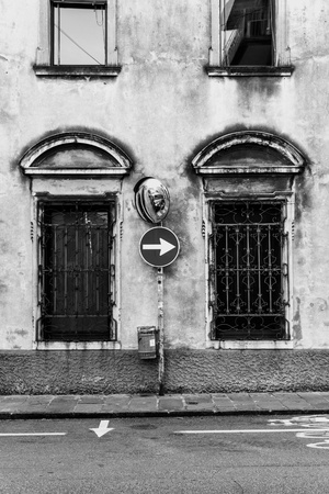 Black and white photo of an arrow traffic sign and a road mirror in an old Italian townの写真素材