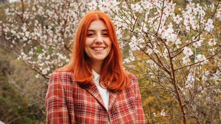 Happy red-haired girl under spring flower tree. Spring mood.