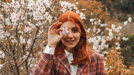Happy red-haired girl under spring flower tree. Spring mood.