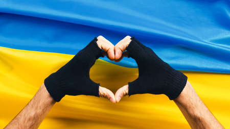 hand in heart shape with ukrainian flag in backgroundの写真素材