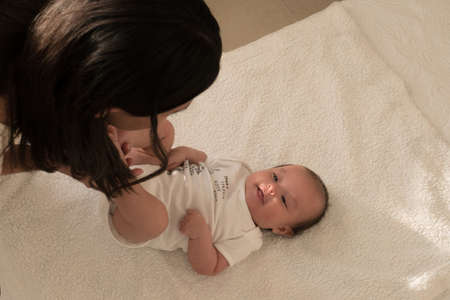 Latin young mother kisses baby feet and sniff them on the bed at homeの写真素材