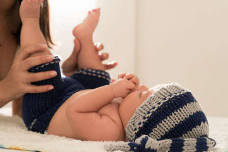 Latin young mother kisses baby feet and sniff them on the bed at home