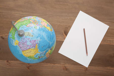 Globe isolated on wooden background and a paper with a penの写真素材